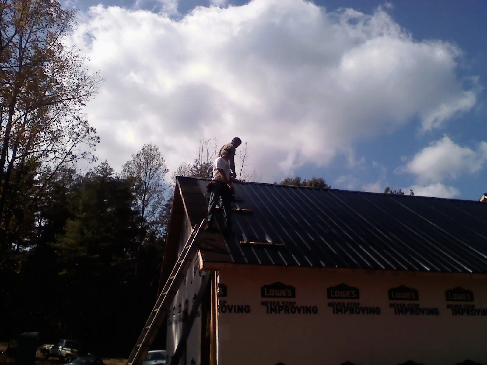 Roofer fastening dark metal panels high against a cloudy sky, from a Roof Inspection job in Glassboro