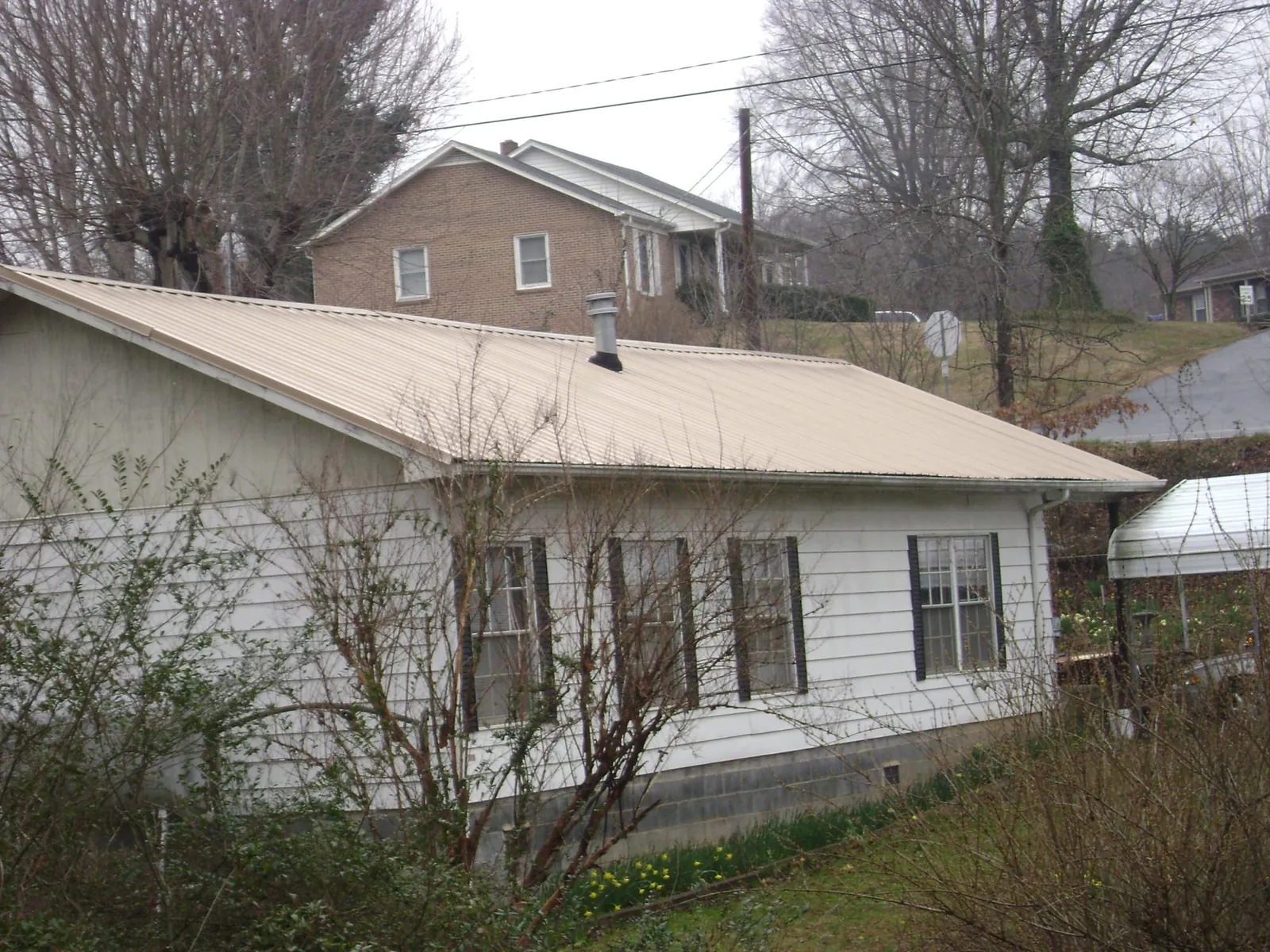 Tan metal roof on a white sided house set into a hillside — Commercial Roofing by Roofing Brothers in Glassboro
